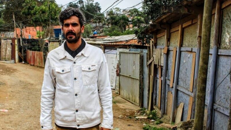 Jaison Lara in front of some rudimentary houses. ara is an environmental activist working on culture and the education of children and young people. Photo by Isabela Alves/Agência Mural, used with permission.