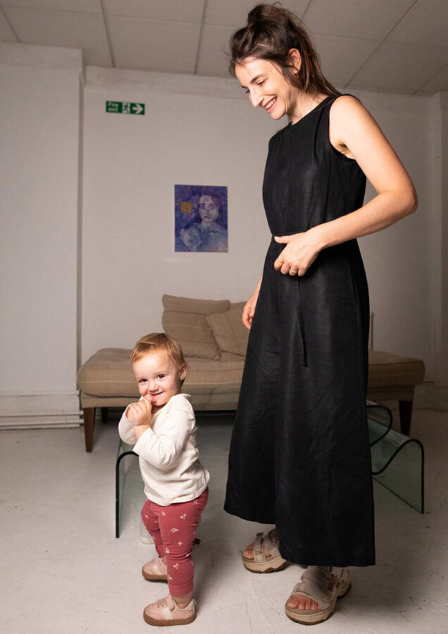 Artist Talia Levitt paints with her newborn resting on her shoulder—a glimpse into the intimate reality behind ‘24/7,’ the body of work shaped in the blur between caregiving and studio practice. Photo courtesy of the artist.